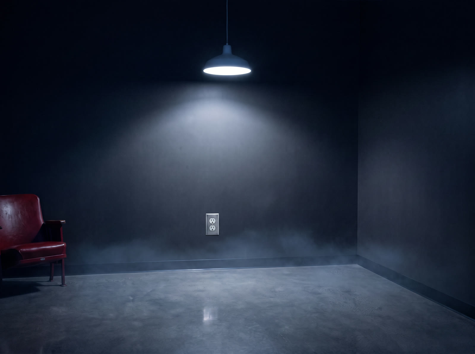 An empty corner of a dark break room, lit by a single lamp, with one wall outlet